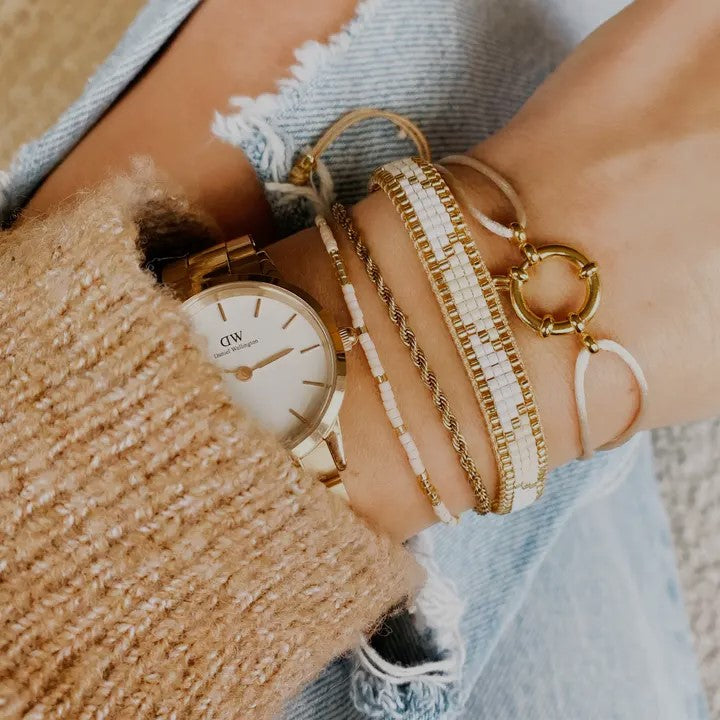 Handgelenk mit mehreren Armbändern in gold und weiß tönen. Elegant und minimalistisch für alltags und schicke outfits.