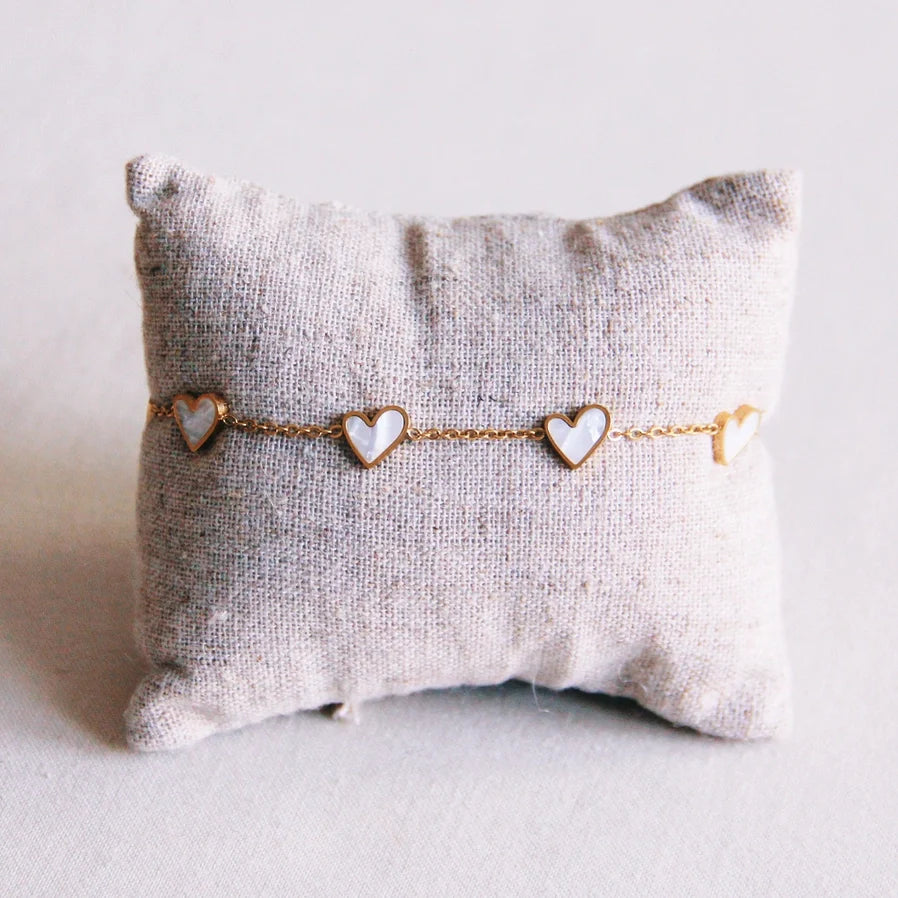 Amrband mit filigraner goldfarbener Kette und mehreren weißen Herzanhängern um ein helles Kissen gespannt. Für einen femininen romantischen Look.
