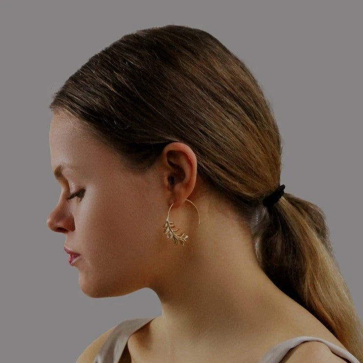 Frau mit einem Pferdeschwanz im Profil. Sie Blickt nach unten und trägt Creoeln mit goldfarbenen Rosmarinzweigen. Perfekt für alle die Schmuck in Natur Optik lieben.