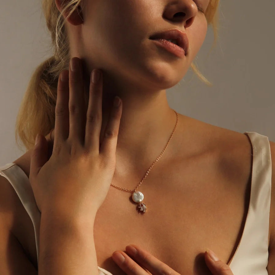 Dekoltee einer Frau mit einer filigranen goldfarbenen Kette. An der Kette hängt eine große Perle und darunter geometrisch angeordnete Kristalle. Für einen eleganten, festlichen Look.