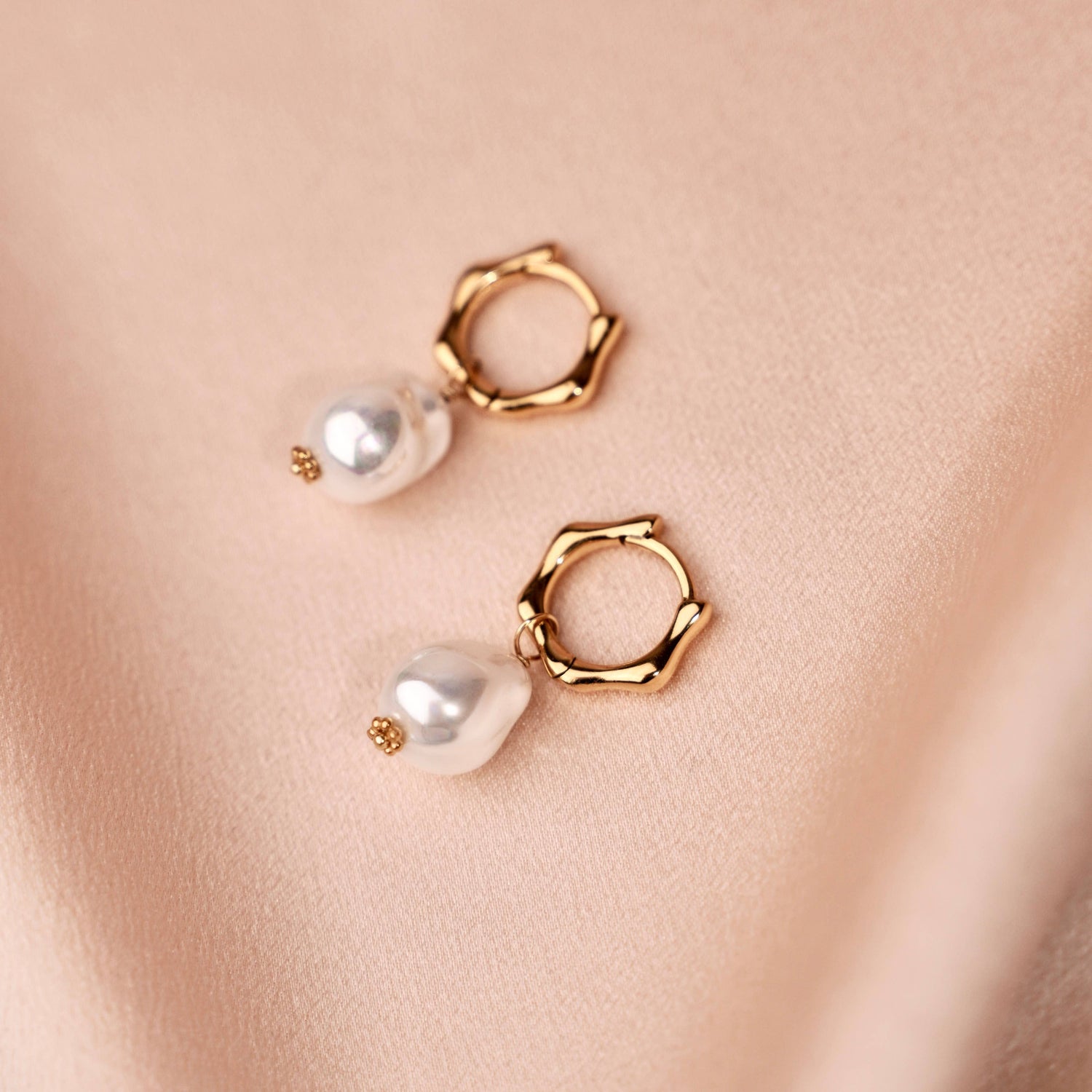 Zwei Ohrringe mit Perlen und eingefassten Kristallen liegen auf einem hellgrünen Buch. Perfekt für einen eleganten und festlichen Look.