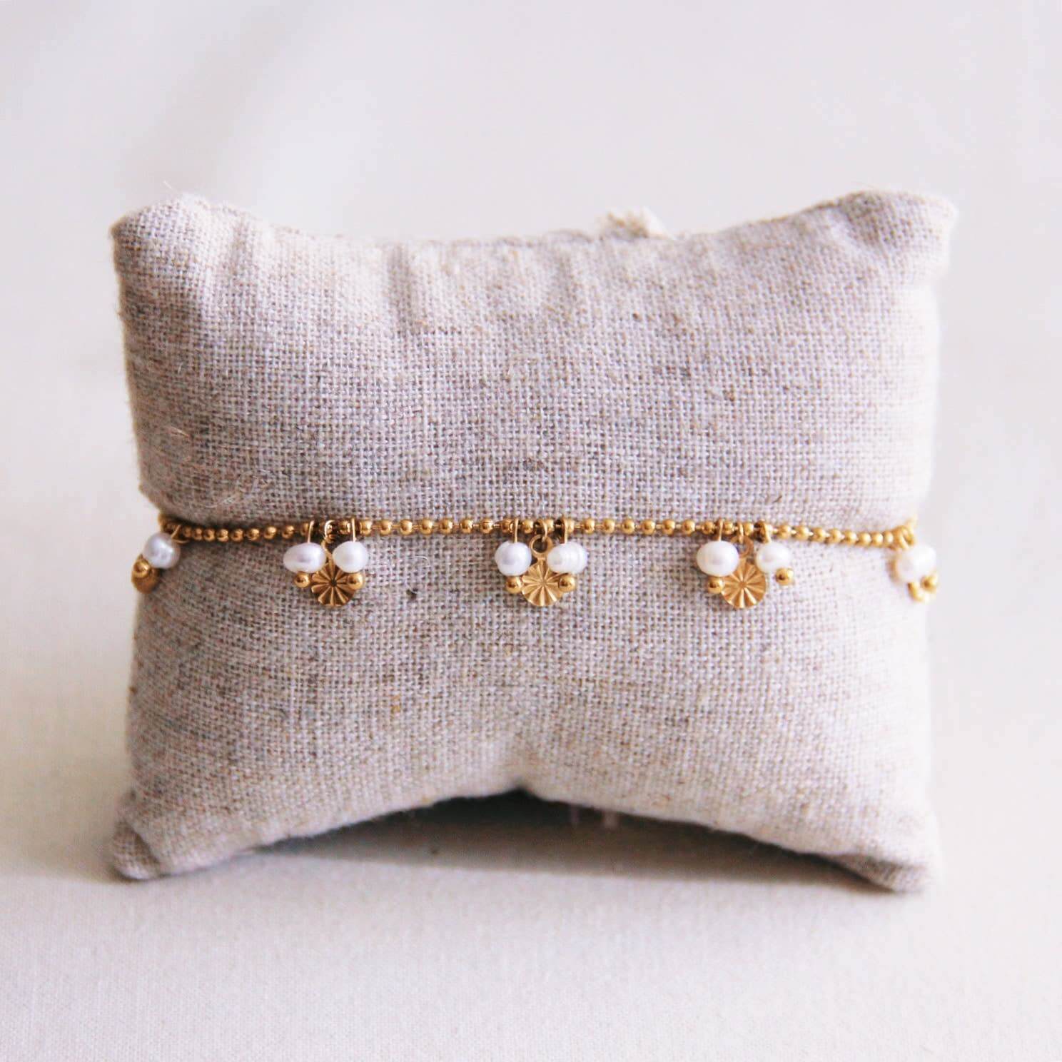 Kugelketten Armband mit runden, goldfarbenen Anhängern und kleinen Perlen, um ein Kissen angebracht. Das Armband ist aus Edelstahl und perfekt zum kombinieren für einen individuellen Look.