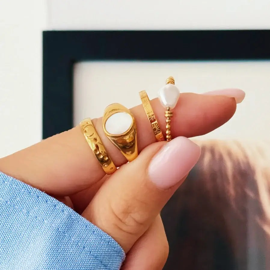 Mehrere RInge auf einem Finger. Darunter ein goldfarbener Ringe mit Kugeln und einer Perle.