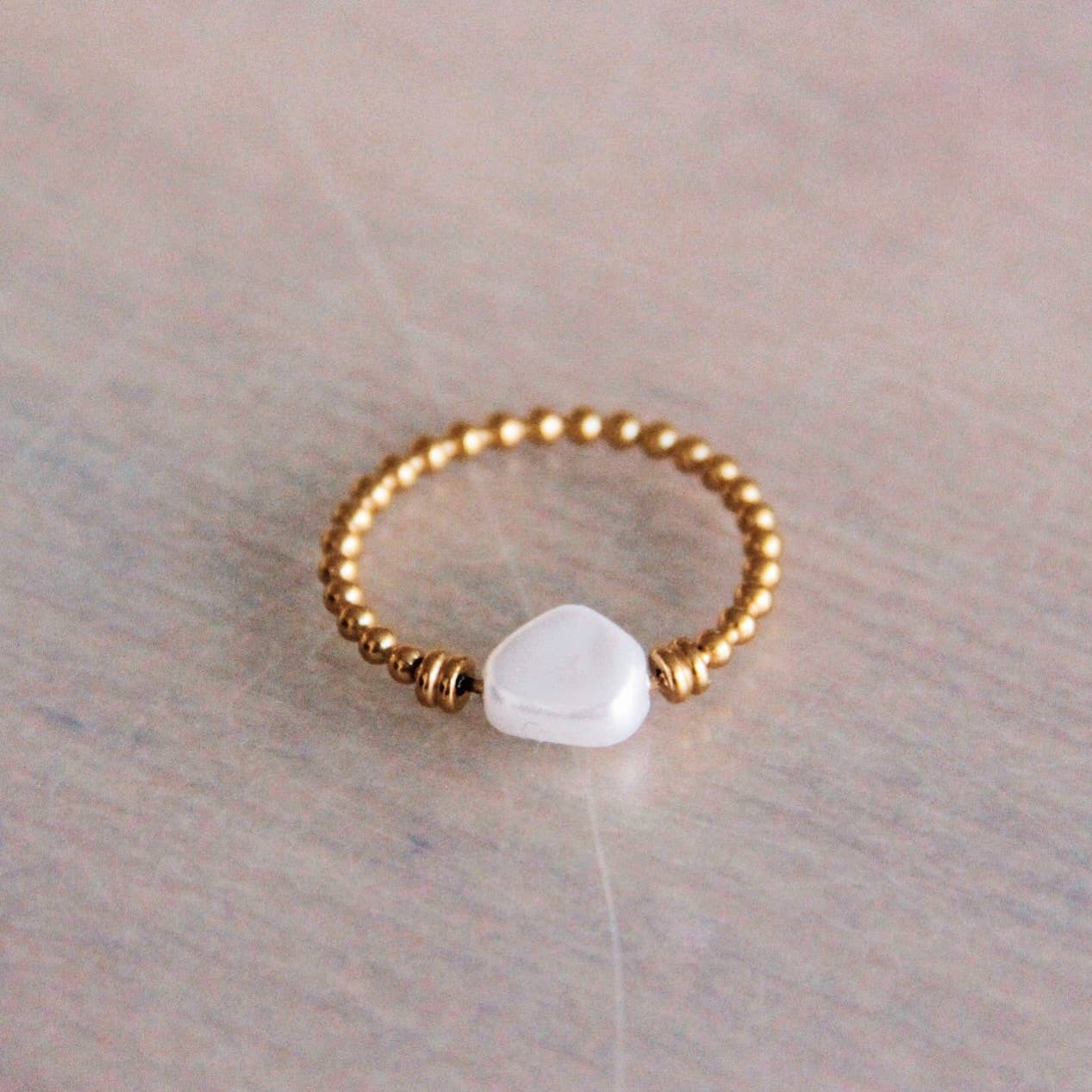 Ring mit golddenen Kugeln und einer Perle. Auf einem beigen Hintergrund von schräg oben. Für einen natürlichen, minimalistischen Look.