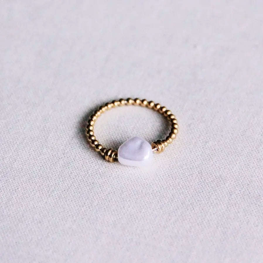 Auf einem weißen Hintergrund liegt ein Ring mit goldenen Details und einer weißen Perle in der Mitte.