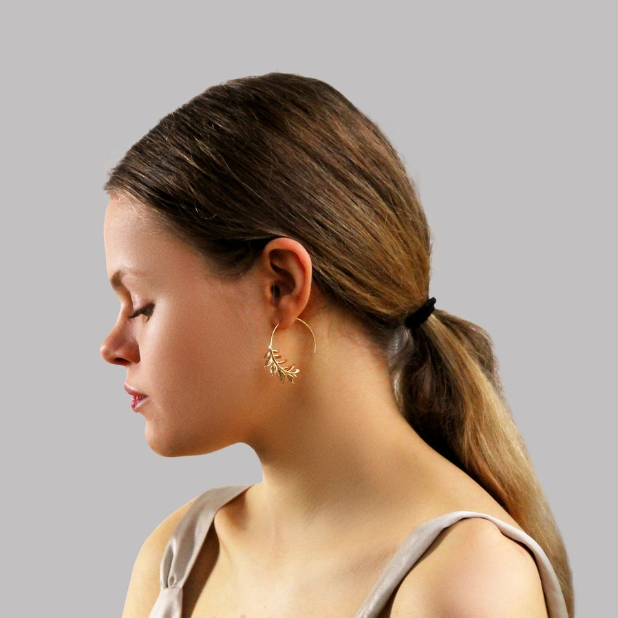Eine Frau im Profil, die einen goldfarbenen Hoop Ohrring trägt, der unten zu einem goldfarbenen Rosmarin zweig wird. Perfekt für alle die gerne Schmuck mit Natur Optik tragen.