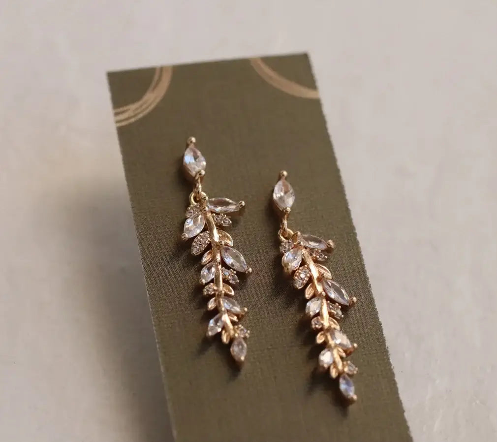 Farnblatt Ohringe mit goldenen, Glasstein und Kristall Details auf einer grünen Karte. Für Frauen mit einem minimalistischen luxeriösen Stil.