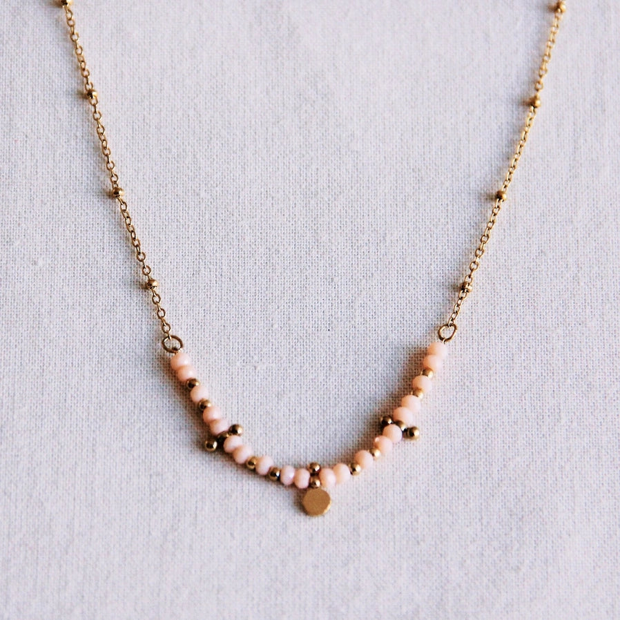 Filigrane goldfarbene Edelstahl Kette mit kleinen rosafarbenen Perlen und goldenen Details. Si eliegt auf einem weißen Hintergrund. Für einen minimalistischen, natürlichen Stil.