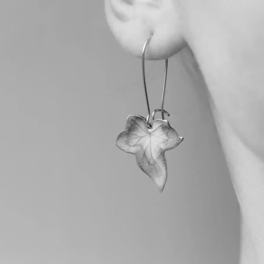 Ein schwarz weiß Bild des Ohres einer Frau, an dem ein Ohrring mit Efeublatt Anhänger hängt.