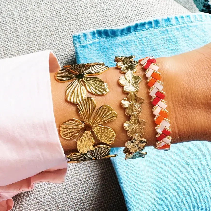 Armreif mit goldfarbenen Blüten aus Edelstahl, kombiniert mit weiteren bunten Armbändern.