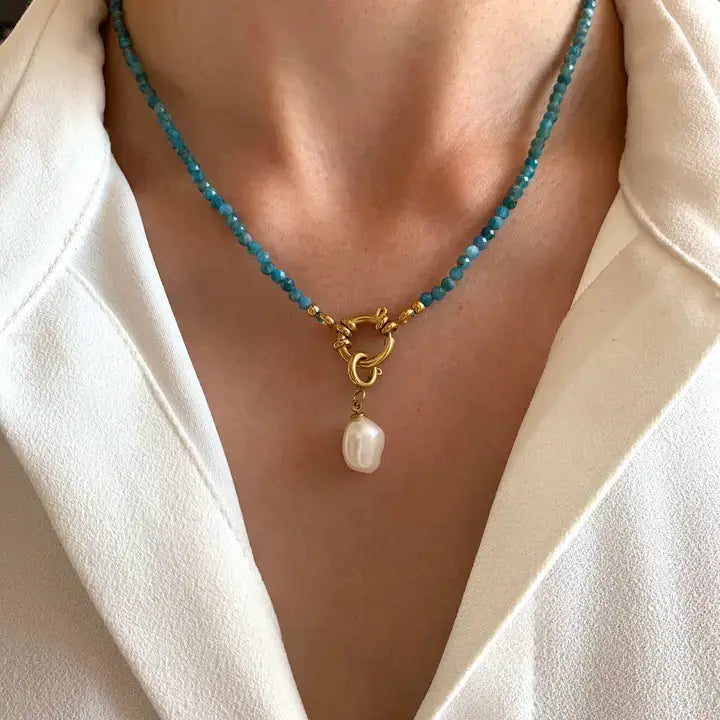Kette aus blauen Natursteinen mit goldfarbenem Edelstahl Anhänger und Perle, getragen um den Hals.