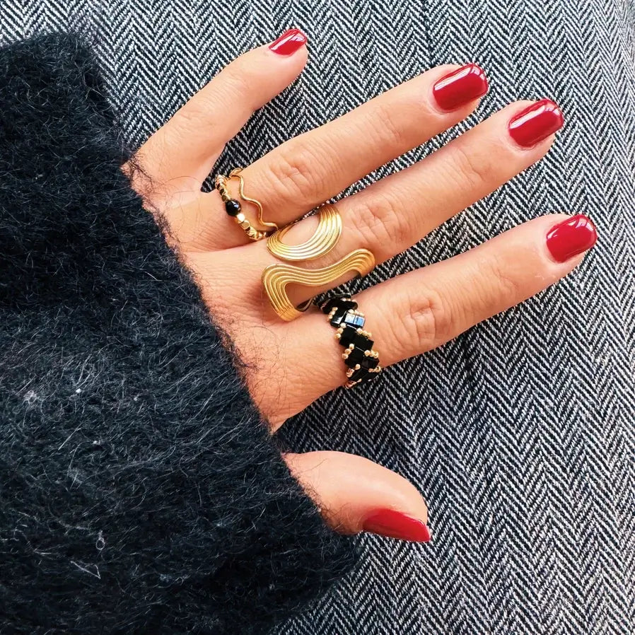 Hand mit lackierten Fingernägeln und mehreren Ringen. Darunter ein großer, auffallender Statement Ring mit Wellenmuster.