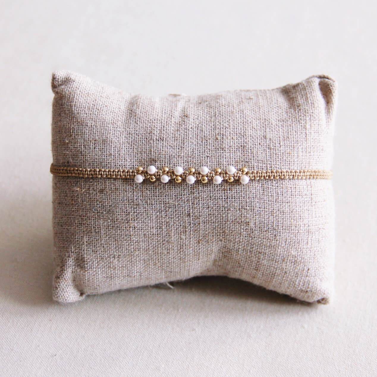 Handgefertigtes Makramee-Armband mit beigefarbener Kordel und eleganten Perlen auf Kissen.