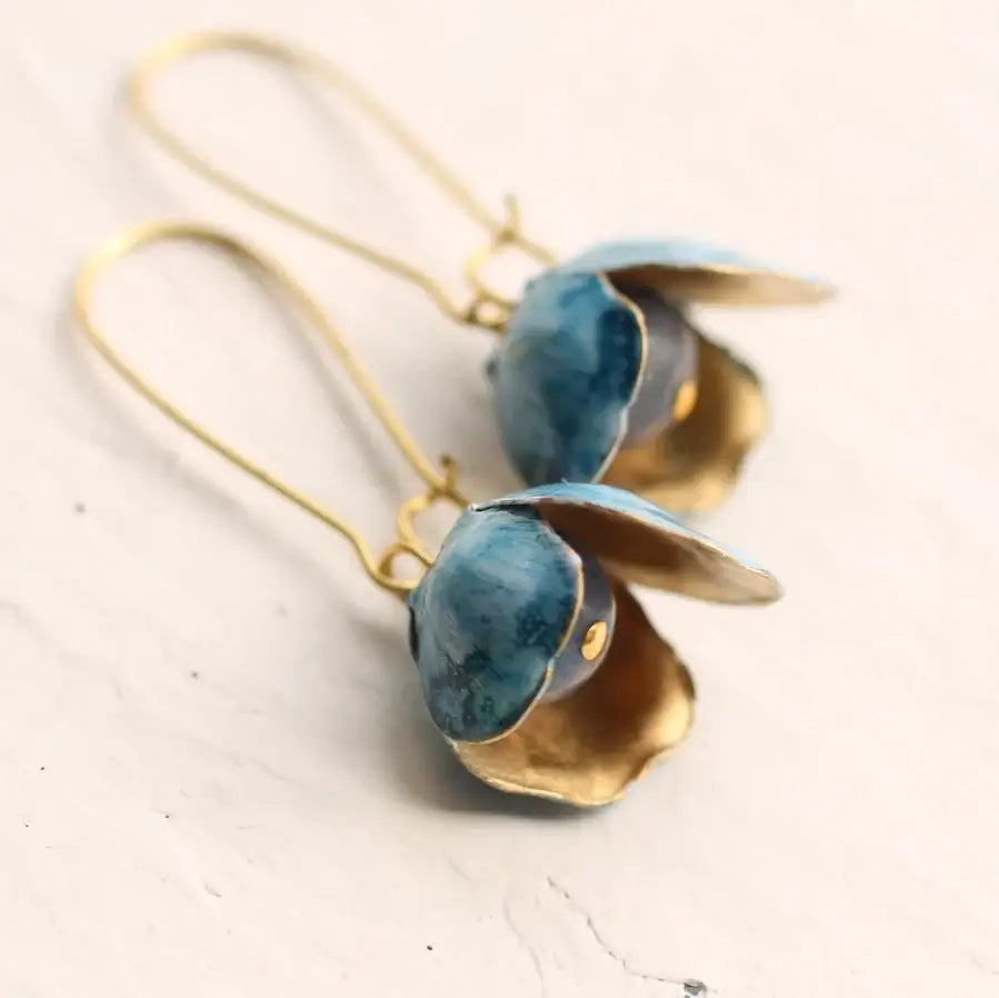 Messing Ohrringe mit handbemalten, blau und weißen Blütenblättern, die innen goldfarben glänzen. In der Mitte sitzt eine Perle. 