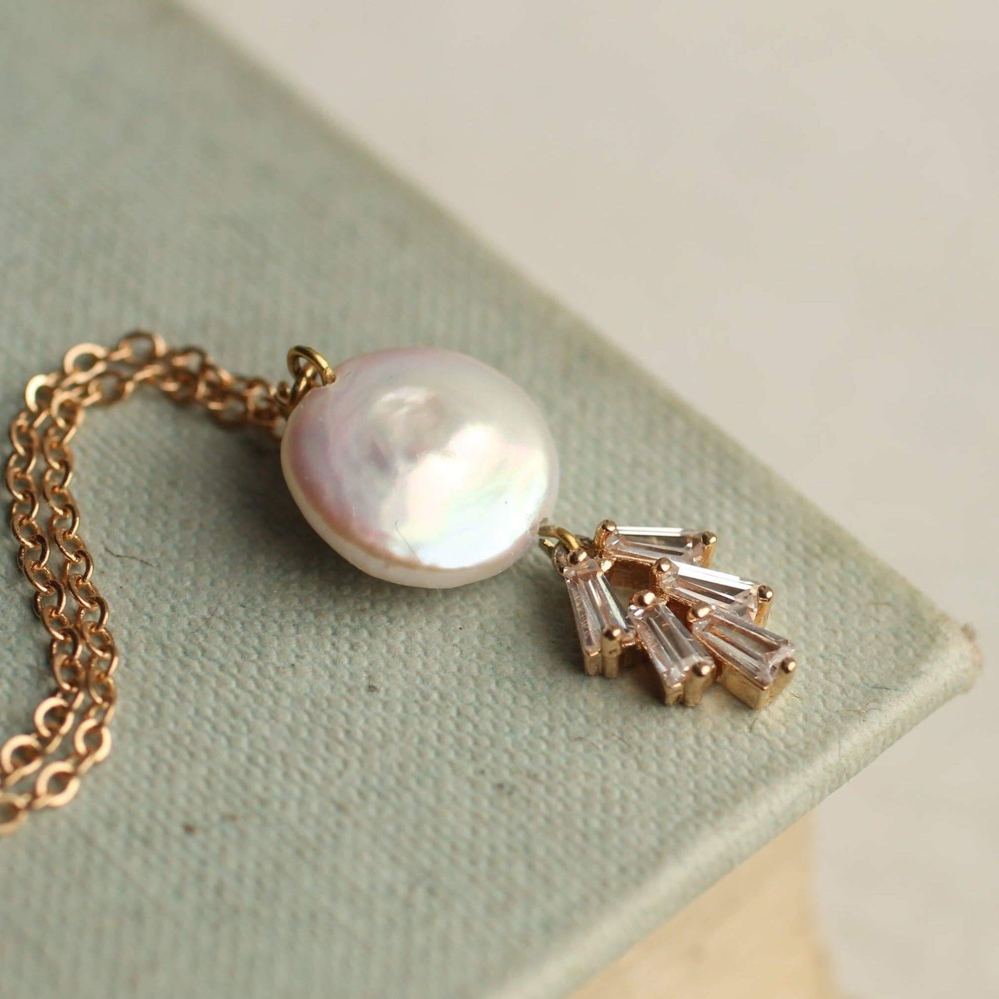 Collana filigranata dorata in stile Art con un pendente a perla e dettagli in cristallo. Su uno sfondo verde.
