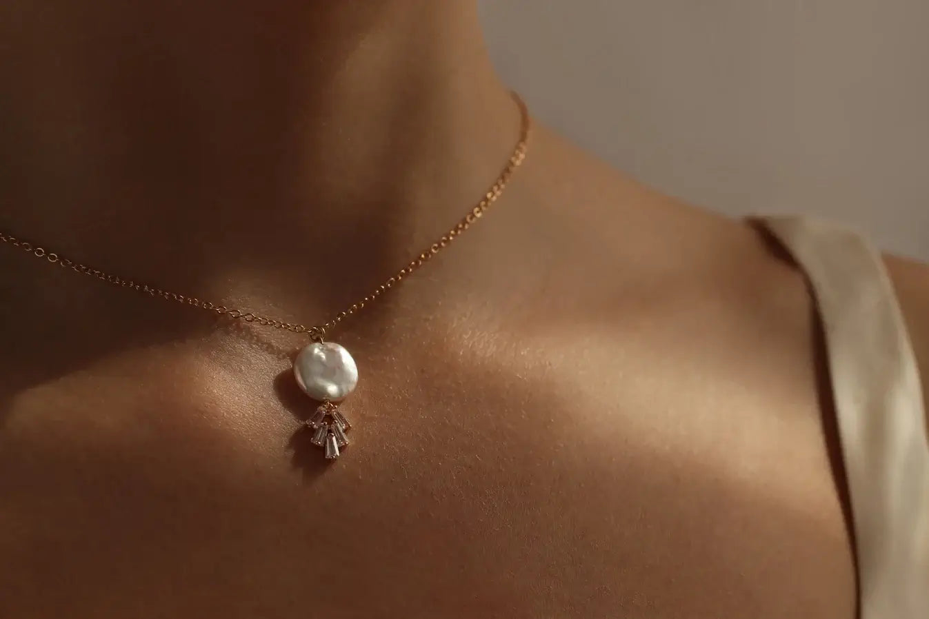 Dekoltee einer Frau mit einer filigranen Kette aus Messing mit einem Perlen Anhänger. Unter der Perle sind diamant artige Steine. Für schicke, elegante Outfits.