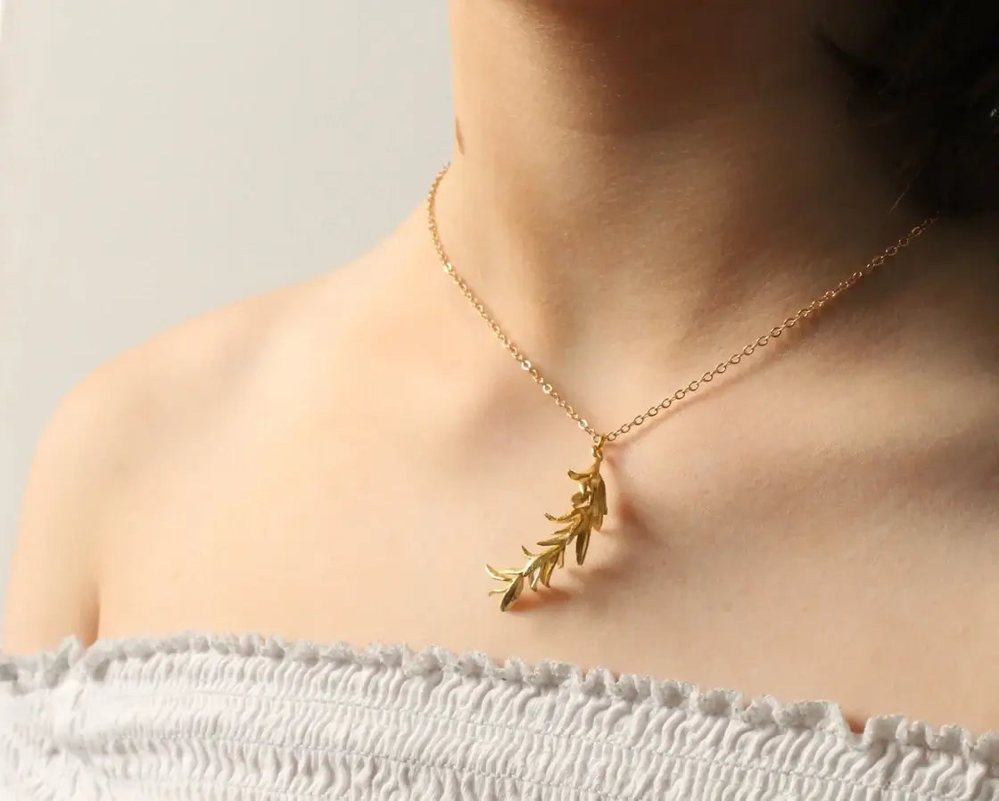 Dekoltee einer Frau, die eine goldfarbene Kette mit einem Rosmarinzweig Anhänger trägt. Der Anhänger ist ca 4,5cm lang und ist perfekt für alle, die Schmuck mit Naturmotiven lieben.