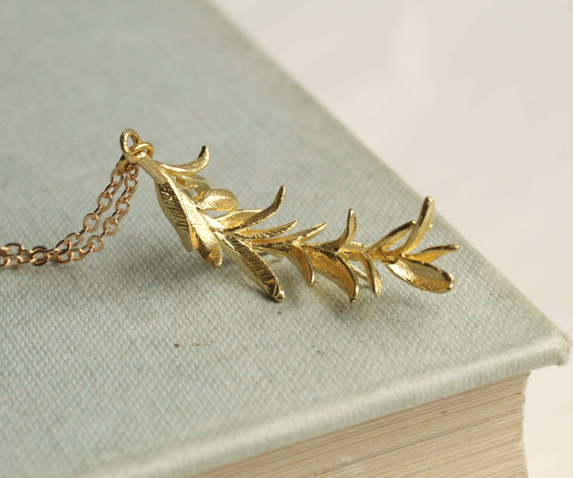 Filigrane goldfarbene Halskette mit einem goldenen Anhänger in Form eines Rosmarinzweigs. Für einen natürlichen eleganten Stil.