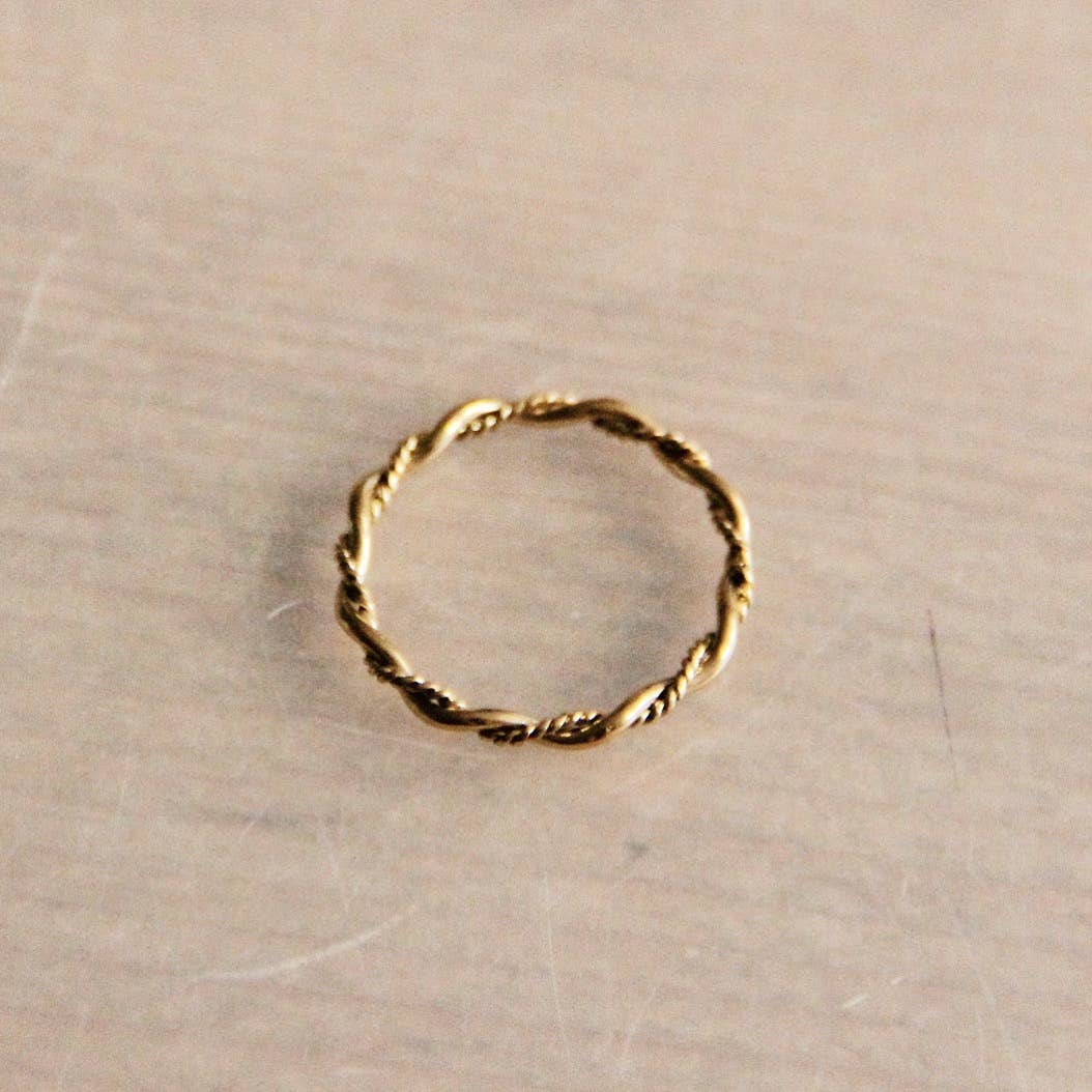Ein geflochtener, schlichter Ring auf einem beigen Hintergrund. Zum kombinieren für einen schicken, einfachen Look.